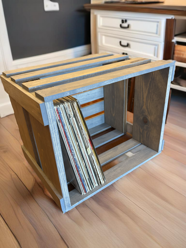 Gray stained vinyl record holder crate with records inside, styled on wood flooring.