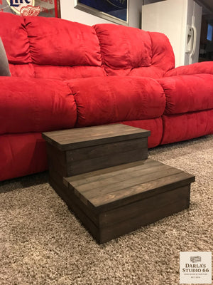 Front angle of a rustic wooden 2-step stool in dark walnut placed by a sofa.