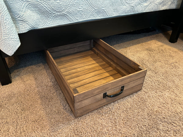 Rustic wooden under-bed storage drawer with black handle pulled out on carpet