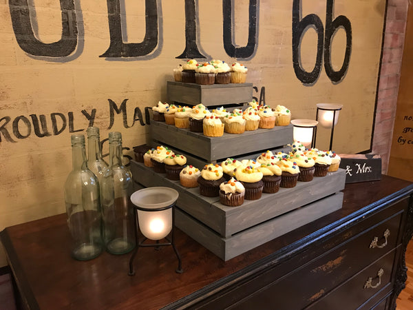 Side angle of antique gray 3-tier cupcake stand with cupcakes displayed on a wooden buffet.