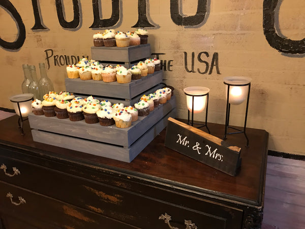 Angled view of rustic 3-tier cupcake stand in antique gray, styled with cupcakes and candles.
