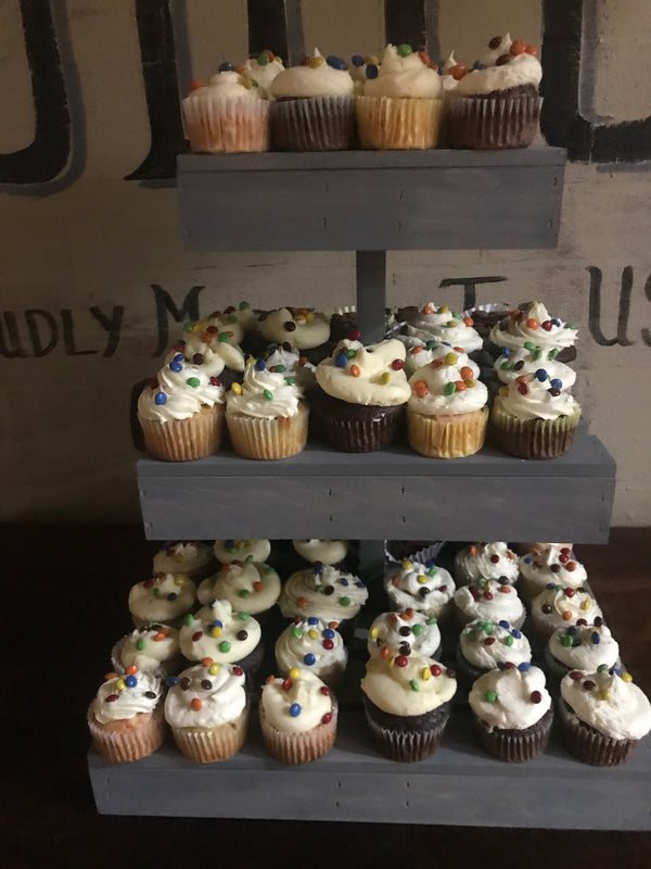 Close-up of rustic antique gray 3-tier wooden cupcake stand filled with cupcakes.