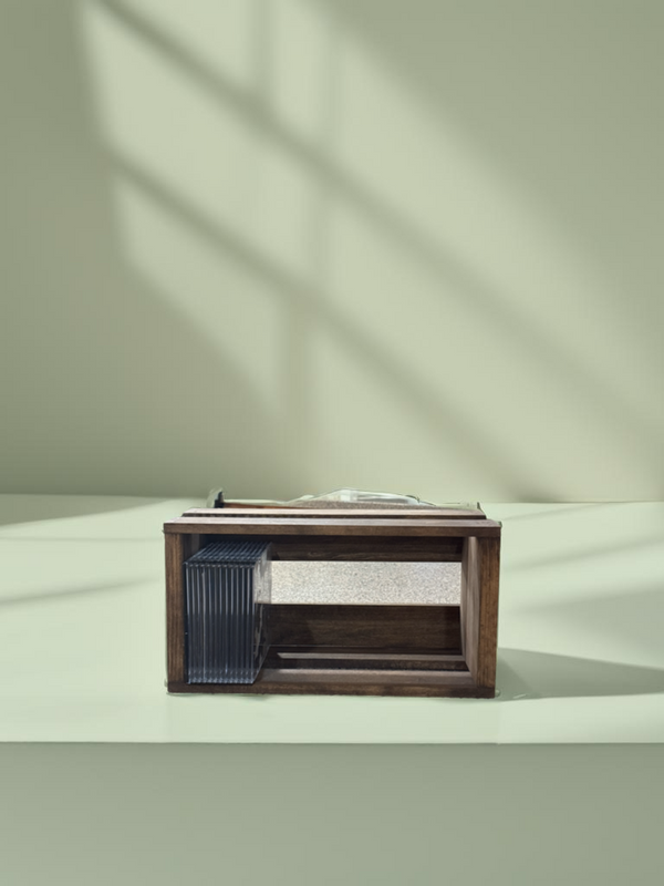 Dark stained wooden CD holder crate on light green table with sunlight shadows.
