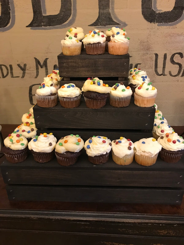 Rustic farmhouse-style dark 3-tier wooden cupcake stand filled with cupcakes in an indoor display.