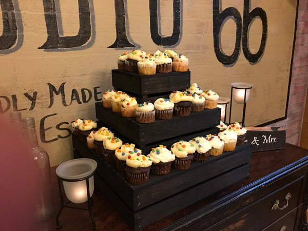 Dark wood 3-tier cupcake stand with cupcakes arranged at an event, side view.