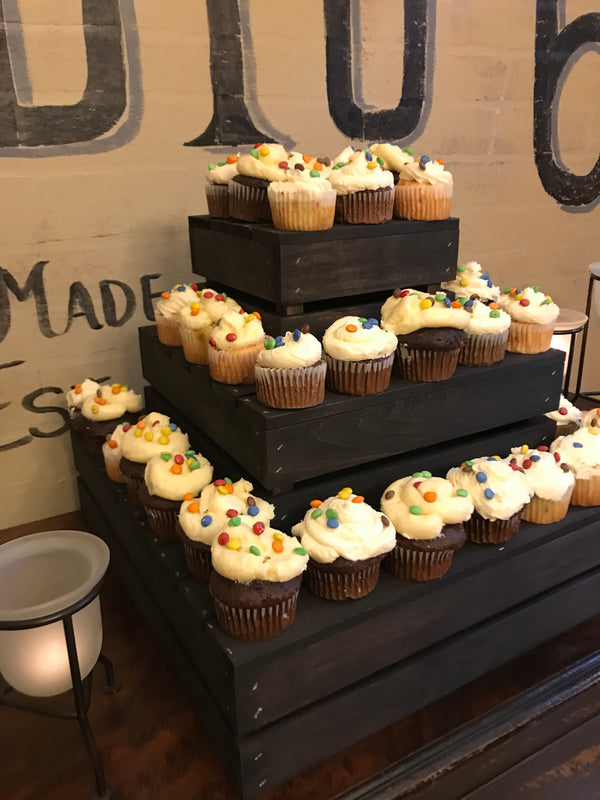 Close-up angled view of a rustic dark stained wooden cupcake stand with cupcakes.