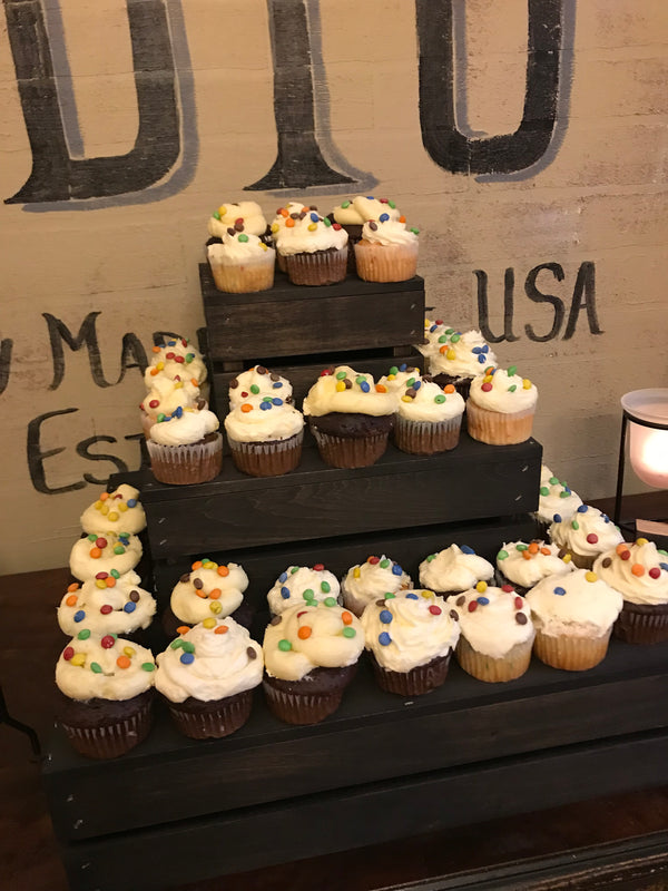 Tiered wooden cupcake display stand in dark stain, decorated with cupcakes at an event.