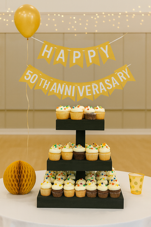Three-tier dark wood cupcake stand displayed at a 50th anniversary celebration with cupcakes and decorations.