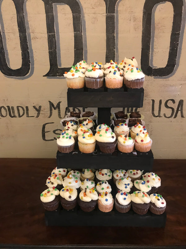Handmade dark wood cupcake stand holding cupcakes at an event with rustic décor and signage.