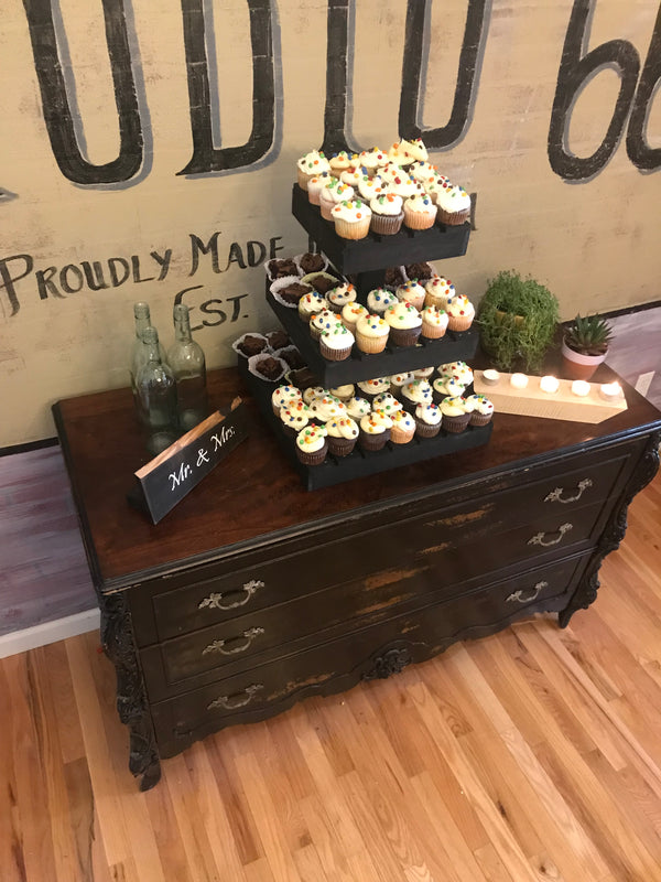 Dark wooden cupcake stand filled with cupcakes at a rustic wedding dessert table with candles and décor.