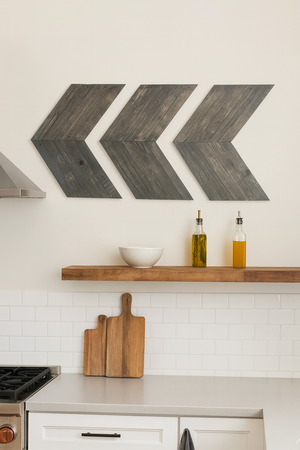 Rustic gray chevron wall art set of 3 mounted above kitchen shelf with cutting boards and oil bottles.