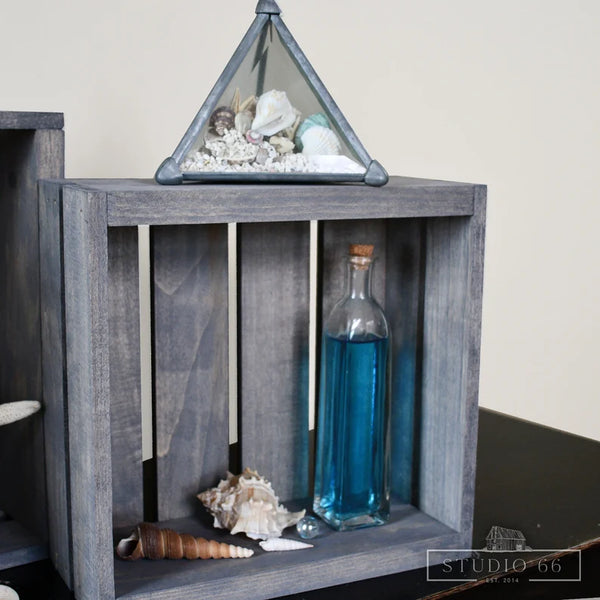 Rustic gray wooden crate used for nautical home decor with seashells and glass bottle.