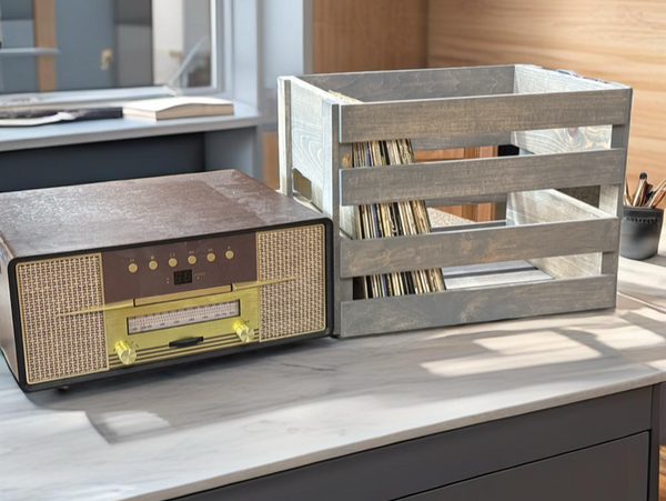 Gray stained wood crate vinyl record holder beside a vintage radio on desk surface.