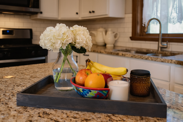 Large gray wood tray on a kitchen counter holding fruit, flowers, and candles for rustic storage.