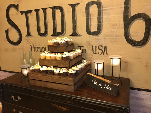 Medium wood cupcake stand with cupcakes in front of Studio 66 rustic wall