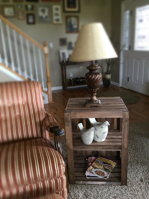 Medium farmhouse wooden end table with lamp, ceramic birds, and magazines for rustic decor.