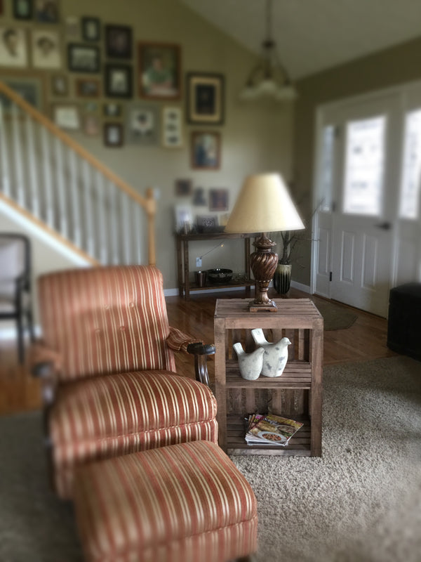 Rustic medium end table with lamp and decor beside striped armchair in farmhouse living room.