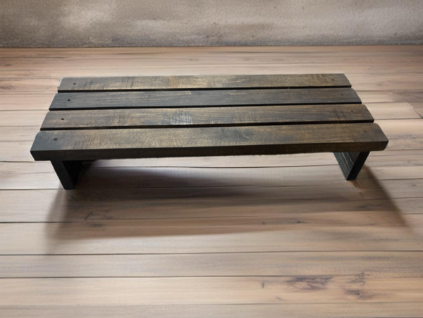 Handmade rustic wooden monitor stand in dark stain shown on wood floor.