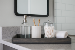 Rustic small gray tray used as bathroom counter organizer with decor items.