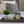 Small gray wooden tray on bed with plant, candle, and alarm clock decor.