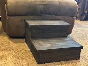 Vintage dark stained 2-step wooden stool beside a couch on carpet, rustic pet stairs or child step stool.
