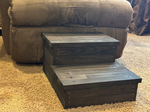 Vintage dark stained 2-step wooden stool beside a couch on carpet, rustic pet stairs or child step stool.