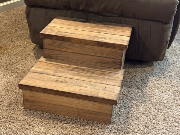 Angled view of rustic 2-tier wooden pet steps in Early American stain against carpet and brown recliner.